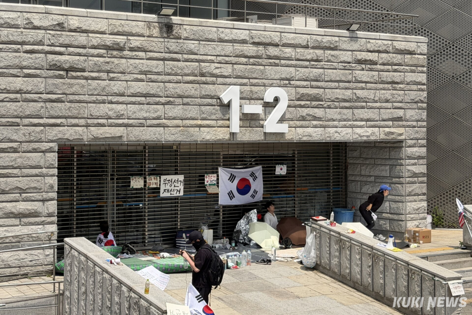 6·3 지방선거 투표용지 부족 사태를 규탄하며 재선거를 요구하는 ‘잠실 개표소 봉쇄 시위’가 계속되고 있는 9일 서울 송파구 올림픽공원 핸드볼경기장 출입구 앞에 시민들이 앉아 투표함 반출을 막고 있다. 유병민 기자